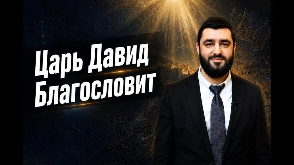 Man in a dark suit with a white shirt and patterned tie stands to the right, in front of a backdrop with large white Cyrillic text that reads “Царь Давид Благословит.”